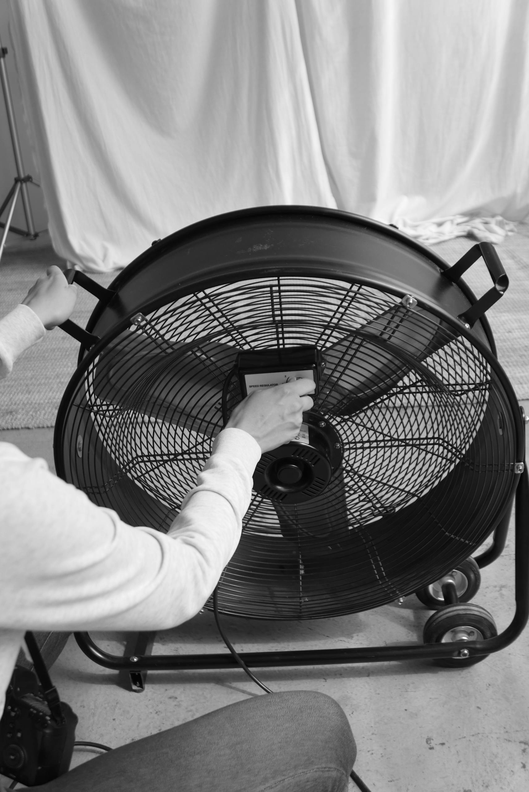 Grayscale image of a person adjusting an industrial fan indoors.